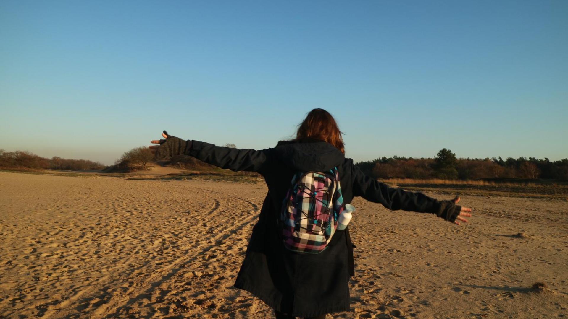 Persoon van achteren gefotografeerd in een zandlandschap.